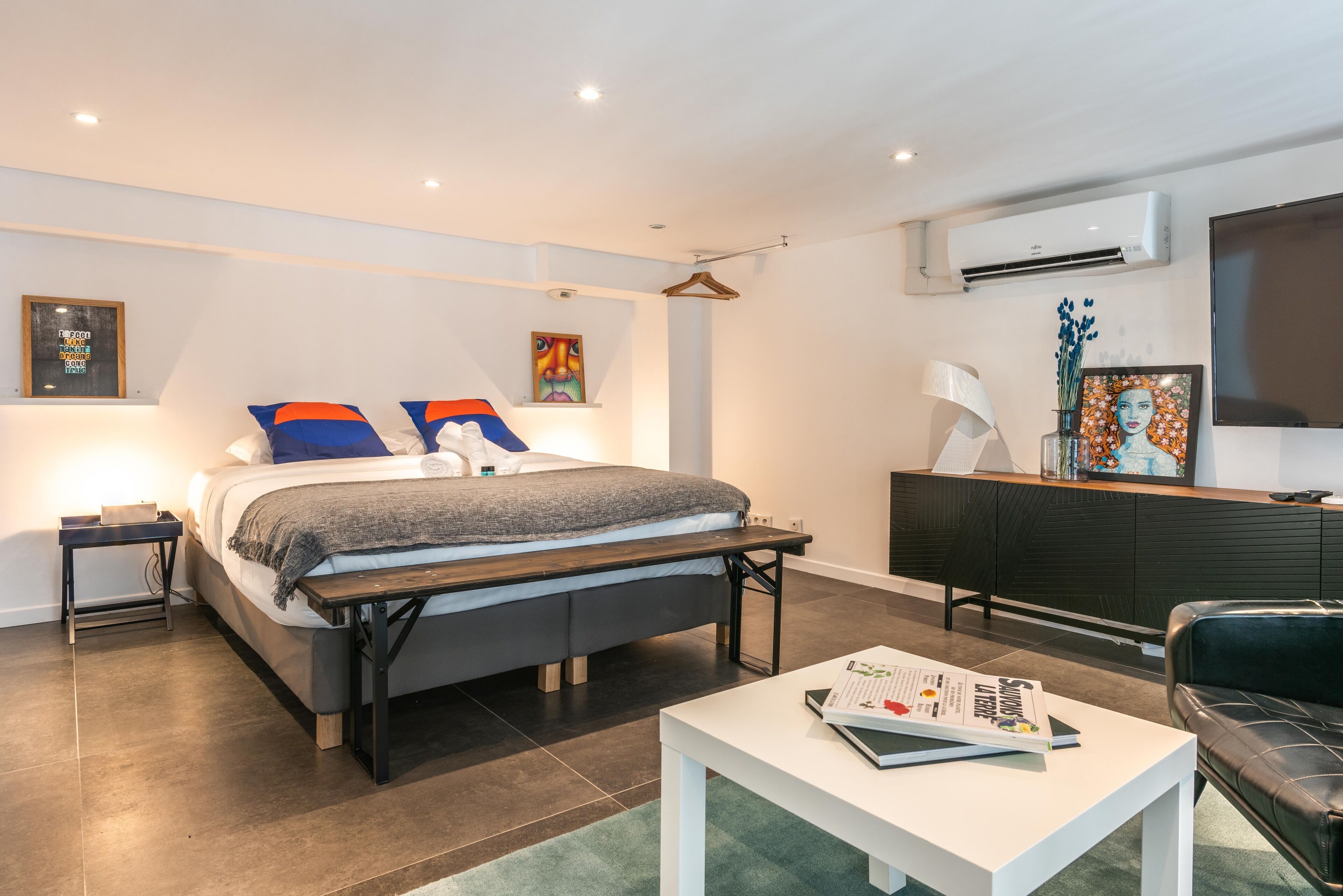 A modern bedroom with a bed, bedside tables, a desk, and a TV.