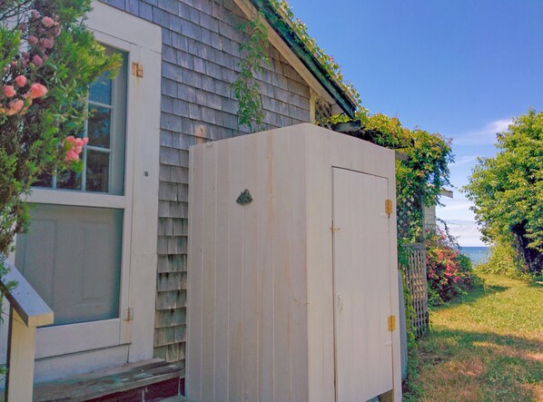 Un cobertizo utilitario blanco al lado de una casa con ventana y puerta.