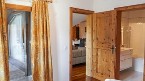 Une pièce avec un plancher en bois, un lit recouvert de draps blancs, une armoire en bois et une salle de bain avec un lavabo et un miroir blancs.