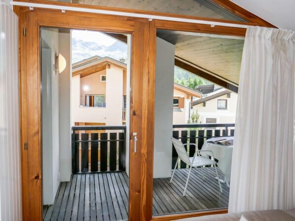A wooden balcony with a view of neighboring houses and a table with chairs.