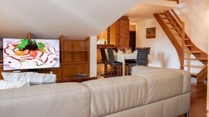 Un salon moderne avec un canapé, un coin repas comprenant une table et des chaises, et un escalier en bois.