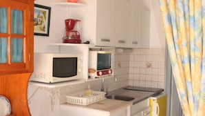 Une cuisine de taille réduite, avec des meubles blancs, un four à micro-ondes, une machine à café et un évier.