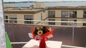 Un balcon avec une table sur laquelle est posé un bouquet de fleurs, donnant sur une étendue d’eau et des bâtiments.