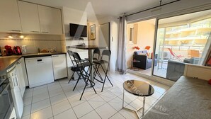 A modern apartment with a kitchen, dining area, and living room. It includes a flat-screen TV, a dining table with chairs, and a sofa.