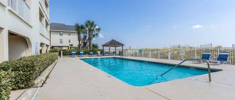 A swimming pool with a sunshade, lounge chairs, and a small gazebo.
