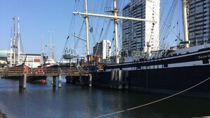 A harbor with a large sailing ship docked at a pier, surrounded by buildings and other boats. - FeWo WeserWeitblick in the 20. Floor in the Columbus Center  (Mitte)