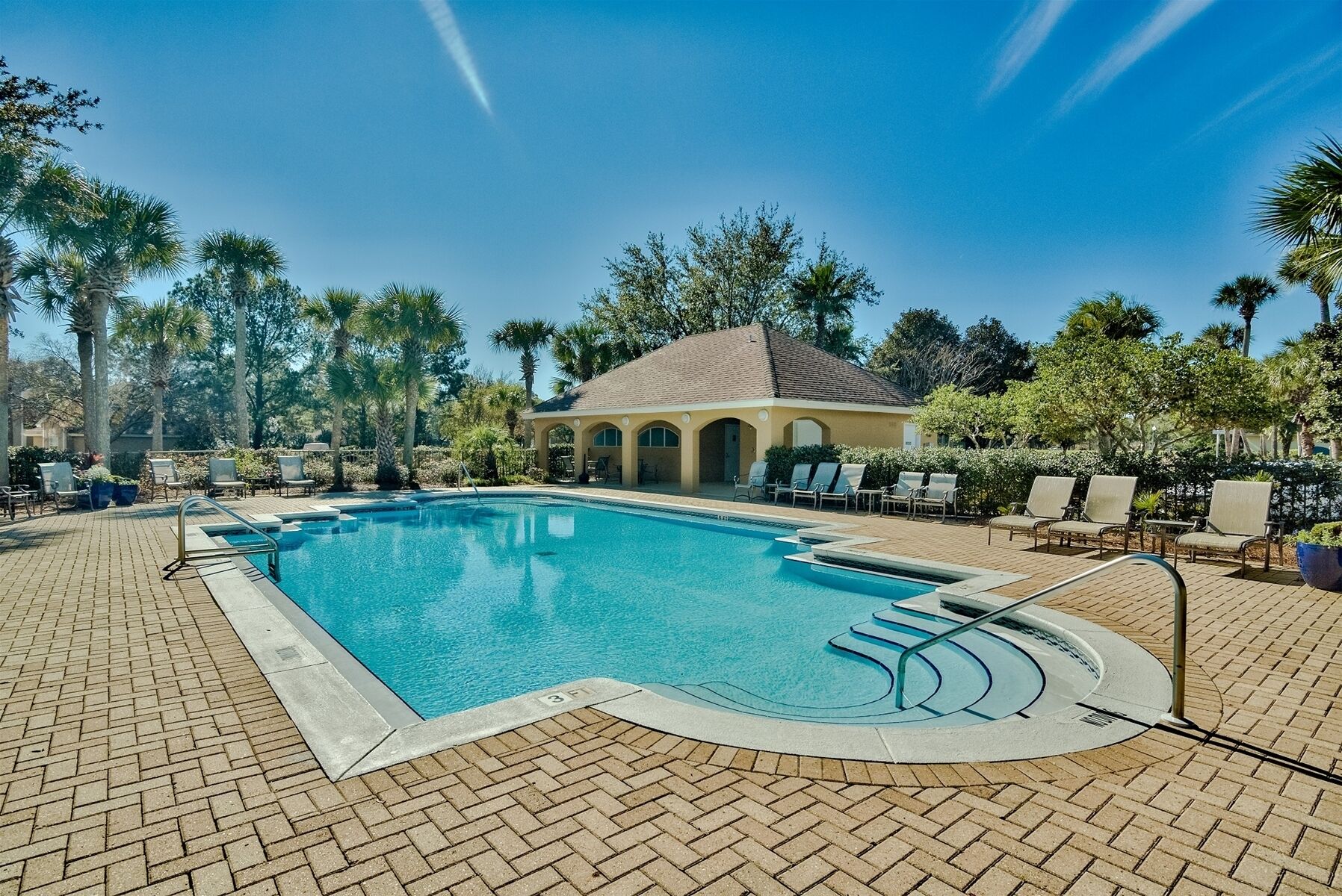 A swimming pool with a sunken hot tub, surrounded by lounge chairs and palm trees.
