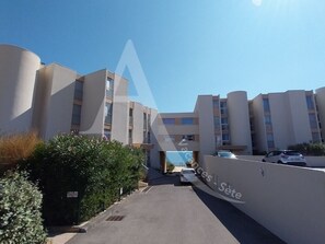 A multi-story residential building with a central entrance, a parking area, and a clear sky. - CONFORTABLE T2 EN FRONT DE MER, PARKING, WI-FI (Sète)