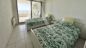 Ein Schlafzimmer mit zwei Betten, einem Balkon mit einem Stuhl und Meerblick.