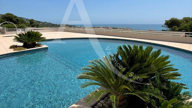 Ein klares, blaues Schwimmbecken mit Blick auf das Meer, umgeben von Grünpflanzen und einer gepflasterten Terrasse.
