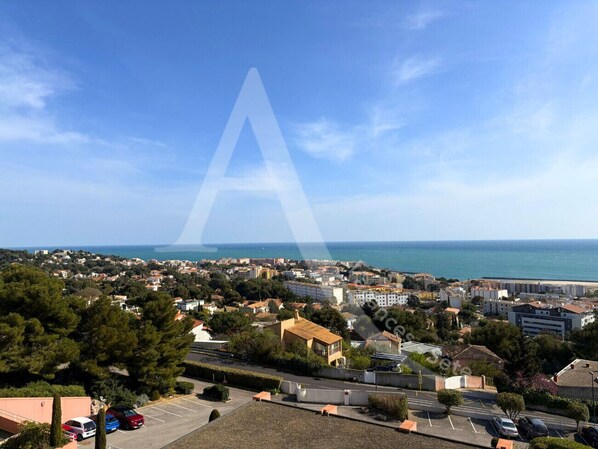 A coastal town with a mix of residential and commercial buildings, a clear sky, and a view of the sea. - 2 CHAMBRES, LARGE TERRASSE VUE UNIQUE, PISCINE, TENNIS (Sète)