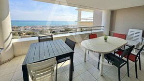 Ein Balkon mit Tisch und Stühlen, Blick auf das Meer und eine Stadt im Hintergrund.
