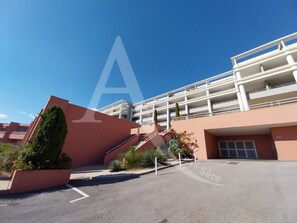 A multi-story hotel with a central staircase, outdoor seating area, and a parking lot. - 2 CHAMBRES, LARGE TERRASSE VUE UNIQUE, PISCINE, TENNIS (Sète)