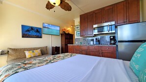 A hotel room with a bed, a sofa, a TV, a kitchen area with a refrigerator, microwave, and coffee maker.