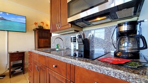 Une cuisine dotée de plans de travail en granit, d’armoires en bois, d’un four à micro-ondes, d’une machine à café et d’un évier.