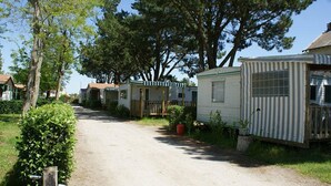 A row of mobile homes with a dirt path in between, surrounded by greenery and trees. - EMPL 3 Mobile home 4 A 6 people (Notre dame de Riez)