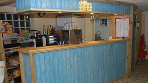 A bar area with a blue counter, various bottles, a clock, and a menu board. - EMPL 3 Mobile home 4 A 6 people (Notre dame de Riez)