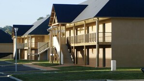 A multi-story motel with a central staircase, outdoor seating, and a parking lot.