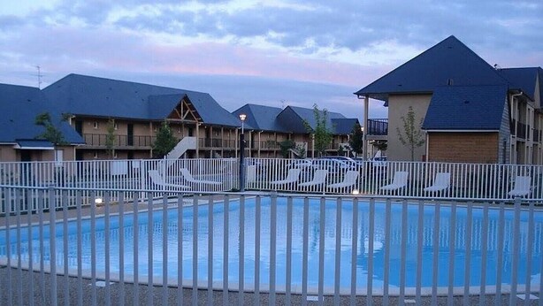 A swimming pool with a white fence, lounge chairs, and a table.