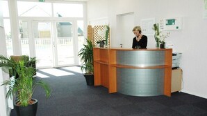A reception area with a wooden desk, two potted plants, and a view of the outside through glass doors.