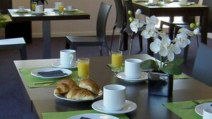A breakfast setup with croissants, coffee cups, and orange juice on a table with green placemats.