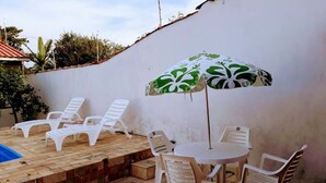 Ein Patio mit weißen Plastikstühlen und einem Tisch, einem Sonnenschirm und einem Swimmingpool.