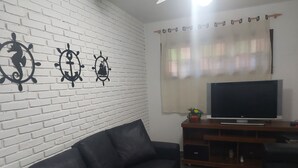 Ein Wohnzimmer mit einer schwarzen Ledersofa, einem Flachbildfernseher auf einem Holzgestell und dekorativer Wandkunst.