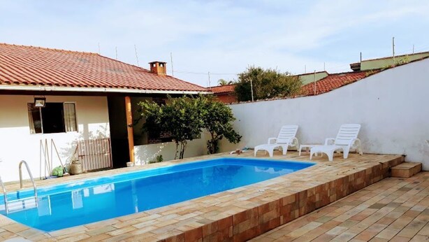 Ein Schwimmbecken mit einer Fliesenveranda, zwei weißen Liegestühlen und einer weißen Wand.