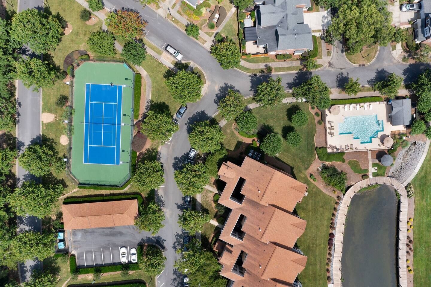 Vista aérea de una zona residencial con cancha de tenis, piscina y estanque.