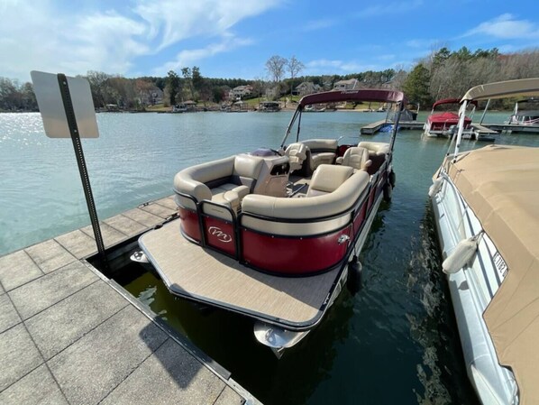 A pontoon boat docked at a marina with a clear view of the surrounding water and houses in the background. - Lake Norman Dream Condo! 1st Floor, Lake View Lake Norman Vacation Rental (Cornelius)