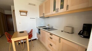 A compact kitchen with wooden cabinets, a sink, a toaster, and a coffee maker. - Cozy apartment near Thermes with balcony, pets allowed (Balaruc-les-Bains)