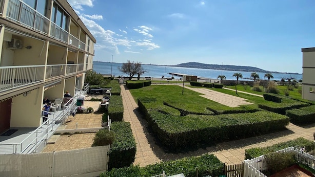 A multi-story building with balconies overlooking a landscaped garden and a body of water. - Cozy apartment near Thermes with balcony, pets allowed (Balaruc-les-Bains)