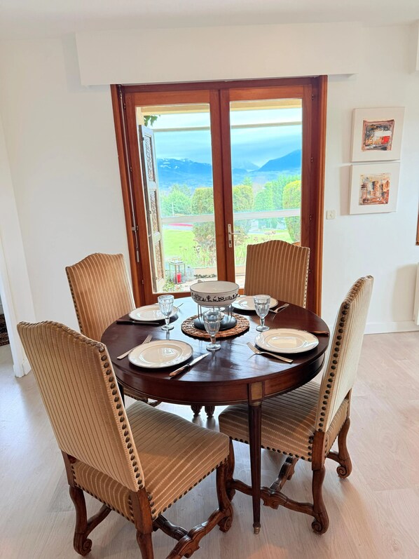 A dining table set for four with chairs, a view through a glass door, and artwork on the wall. - Homerez - House in Reignier-Esery (Reignier-Esery)