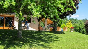 A covered outdoor seating area with chairs and tables, surrounded by lush greenery and trees. - Homerez - House in Reignier-Esery (Reignier-Esery)