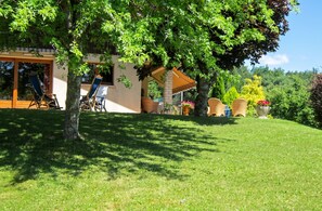 A covered outdoor seating area with chairs and tables, surrounded by lush greenery and trees. - Homerez - House in Reignier-Esery (Reignier-Esery)