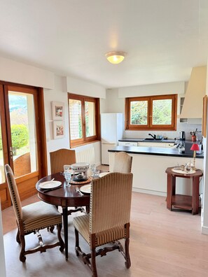 A dining area with a wooden table, chairs, and a kitchen in the background. - Homerez - House in Reignier-Esery (Reignier-Esery)