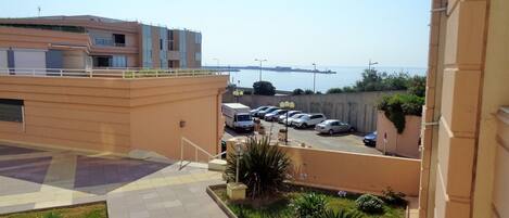 A parking area with several cars, a building with a flat roof, and a view of the sea.