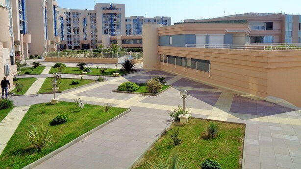 Un complexe résidentiel moderne comprenant plusieurs immeubles d’appartements, une cour intérieure agrémentée de verdure et une promenade piétonne.