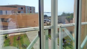 Une vue depuis une fenêtre donnant sur un parking avec des voitures, un bâtiment et un ciel dégagé.