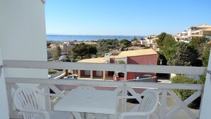 A balcony with a table and two chairs, overlooking a coastal town with buildings and a clear sky.