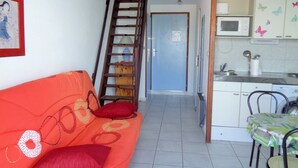 A compact living space with a sofa, a ladder, a kitchen area, and a door leading to another room.