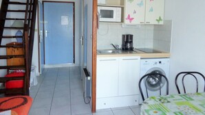 A compact kitchen with a microwave, coffee maker, and a washing machine. A dining area with a table and chairs is visible.