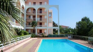 A swimming pool with a white railing, surrounded by a multi-story building with balconies and a palm tree.