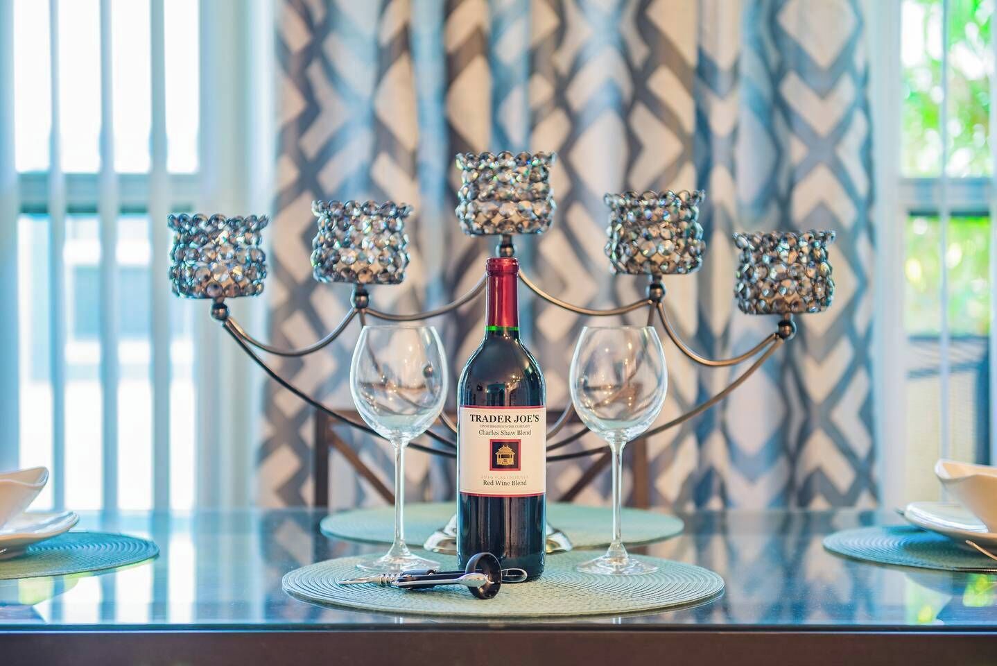Une bouteille de vin sur une table, accompagnée de deux verres et d’un stylo, le tout entouré de bougeoirs décoratifs.
