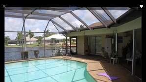A swimming pool with a glass enclosure, a covered patio area, and a view of a lake. - Beautiful View of Intersecting Canals from the Moment You Walk In (Cape Coral)