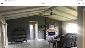 A spacious living room with a stone fireplace, a large window, and a ceiling fan. - Beautiful View of Intersecting Canals from the Moment You Walk In (Cape Coral)