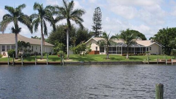 A waterfront property with a house, a dock, and palm trees. - Beautiful View of Intersecting Canals from the Moment You Walk In (Cape Coral)