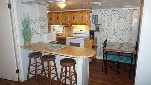 Una cocina compacta con armarios de madera, una estufa blanca y una pequeña isla con taburetes.