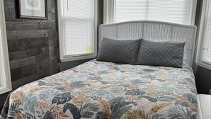 Un dormitorio con colcha estampada de flores, cabecera de mimbre y paredes de madera.