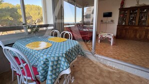 A dining area with a table set for two, a glass door leading to a balcony, and a view of the outdoors.